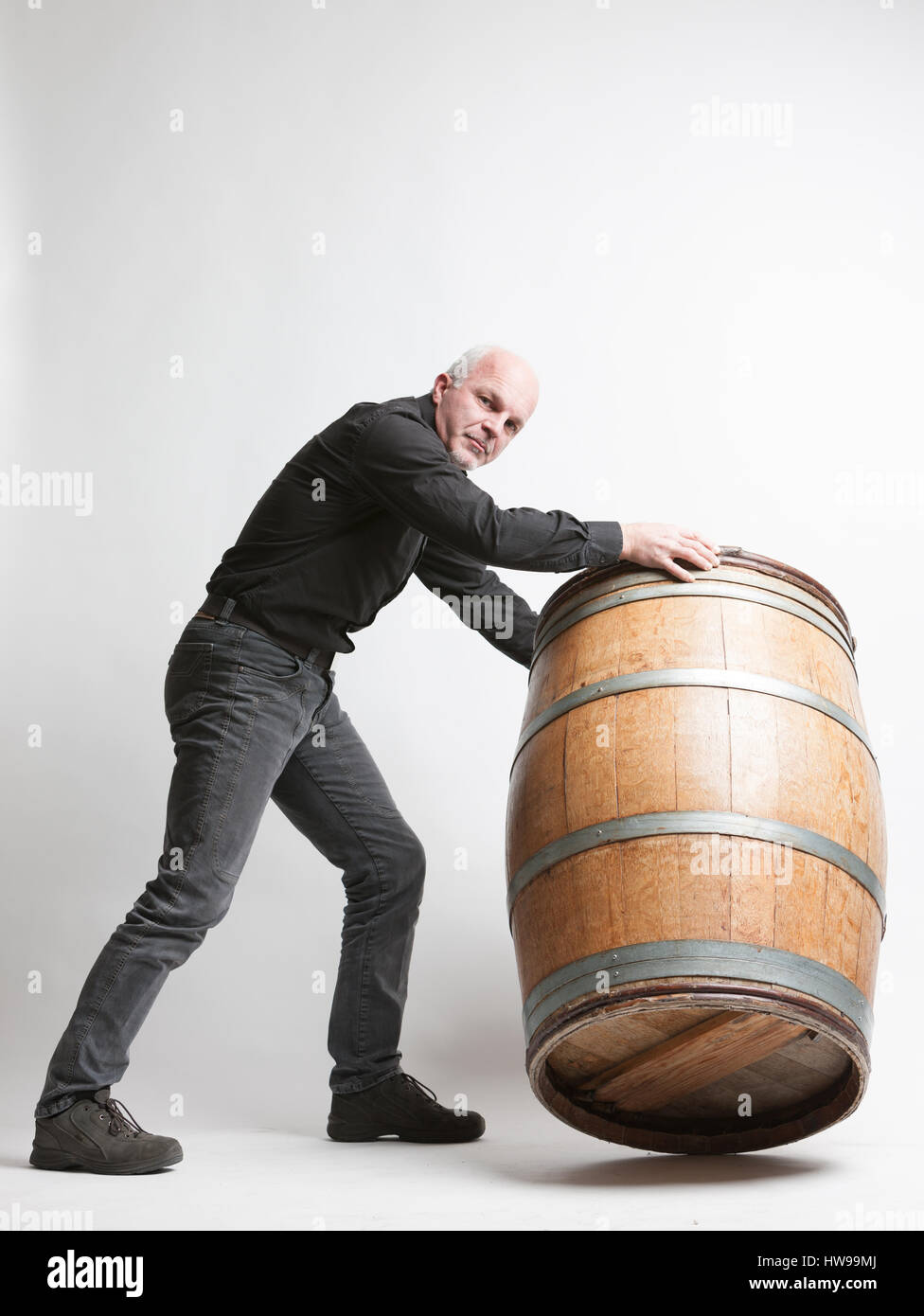 Déplacement d'un homme grand chêne vin ou bière baril en la roulant autour de sa circonférence de base de l'appareil photo avec un air sérieux dans un vitic Banque D'Images