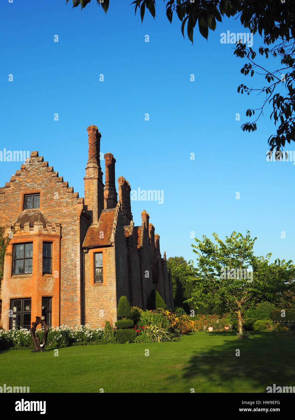 Chenies Manor House montrant les cheminées Tudor contre un ciel bleu. Pelouse et arbres y compris le mûrier par le parterre. Banque D'Images