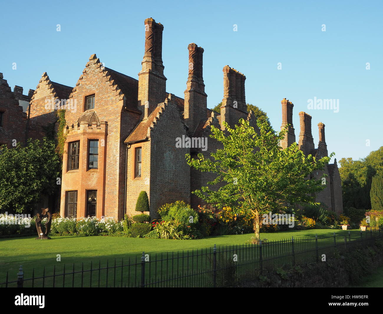 Chenies Manor House montrant les cheminées Tudor contre un ciel bleu. Pelouse et arbres y compris le mûrier par le parterre. Banque D'Images