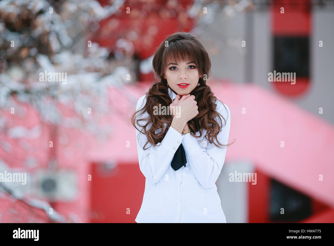 ,Femme,femme,étudiant modèle avec cure,sourire blanc,chemise blanche,prenez,embrasser les mains elle-même,background,arbres,snowflackes avec neige, cheveux bouclés, rouge Banque D'Images