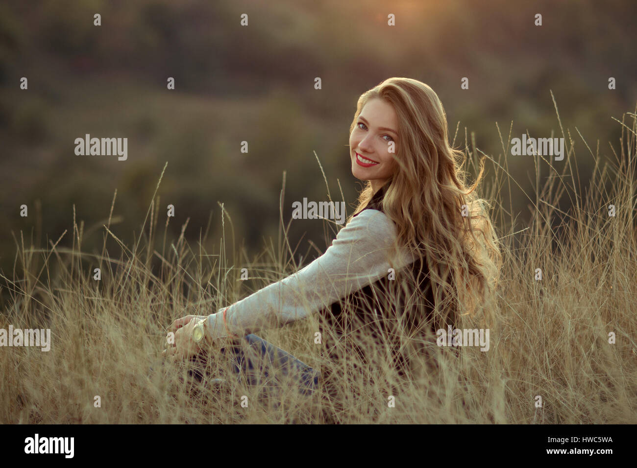 Joyeux joyeux Happy smiling girl sitting on the hill avec très belle vue, incroyablement regarder le coucher du soleil.Beautiful Girl sitting Piscine,en montagne,su Banque D'Images