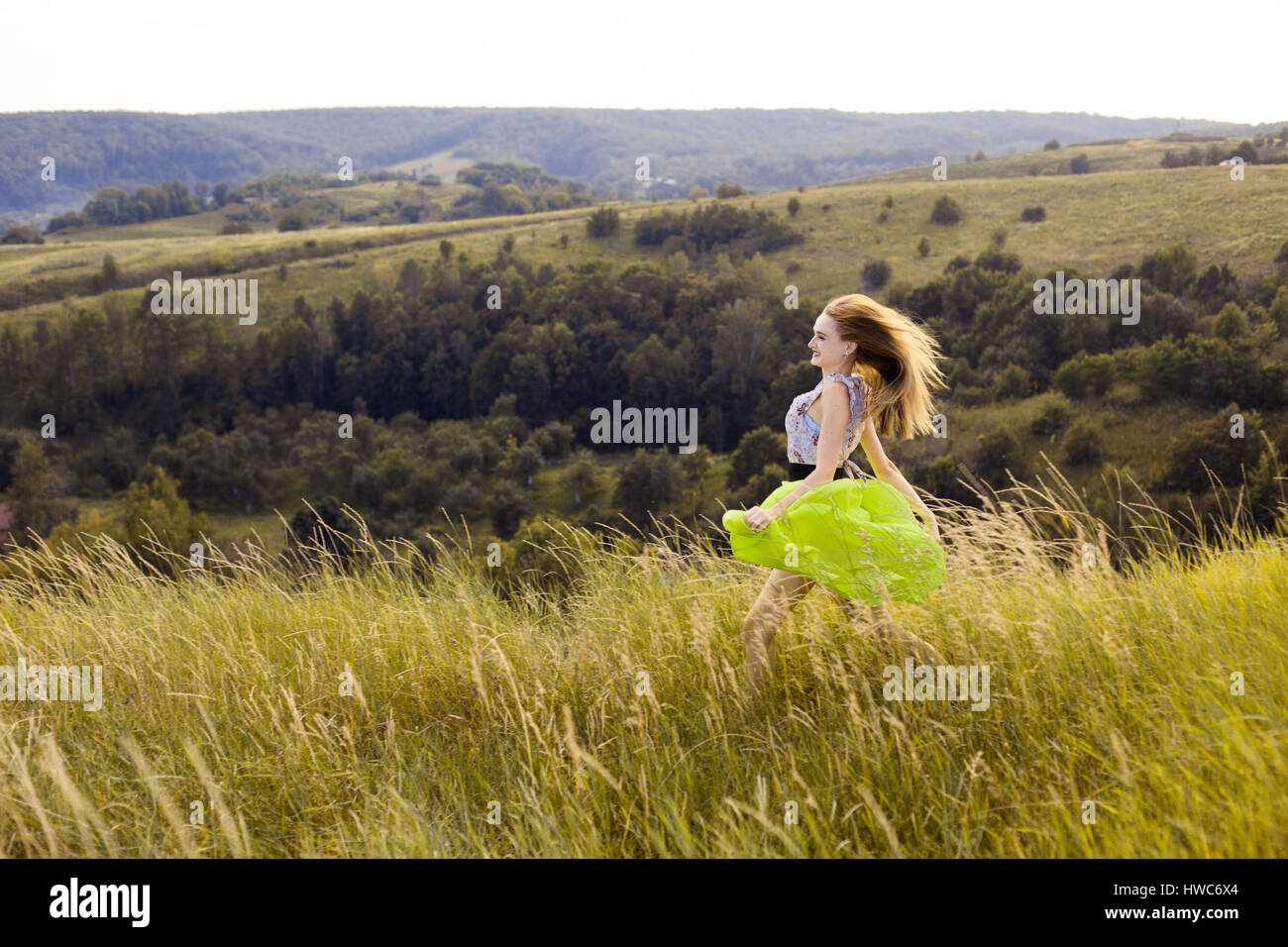 Happy smiling bénéficiant d'été la nature fille courir en été sunny meadow field full blés, fleurs. En été fille robe légère fonctionnant en collines, moun Banque D'Images
