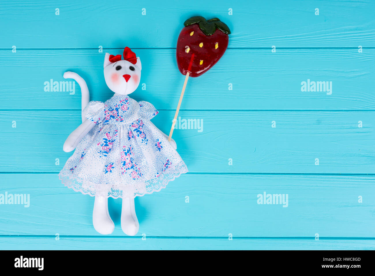 Jouet fait maison sous la forme d'un chat dans une robe colorée comme une sucette holding strawberry on board turquoise en bois Banque D'Images