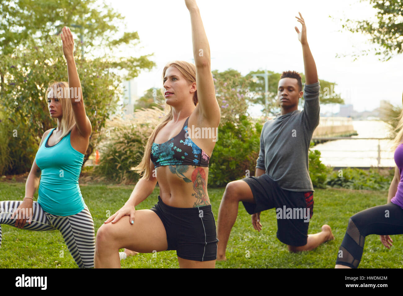 Les hommes et les femmes pratiquant le yoga posent un genou à terre dans le parc Banque D'Images