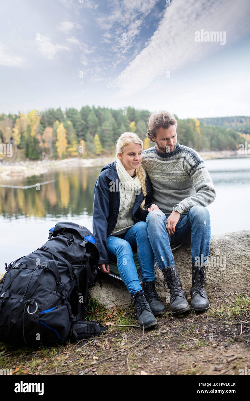 Sac à dos avec couple relaxing on lakeshore pendant camping Banque D'Images