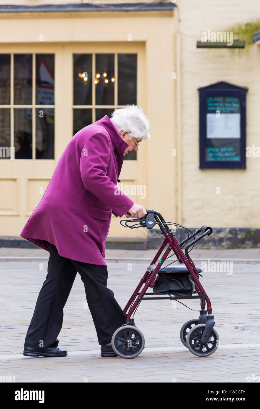 Femme âgée poussant le long du châssis à l'aide à la mobilité partager l'espace salon à Cirencester, Gloucestershire en Mars Banque D'Images