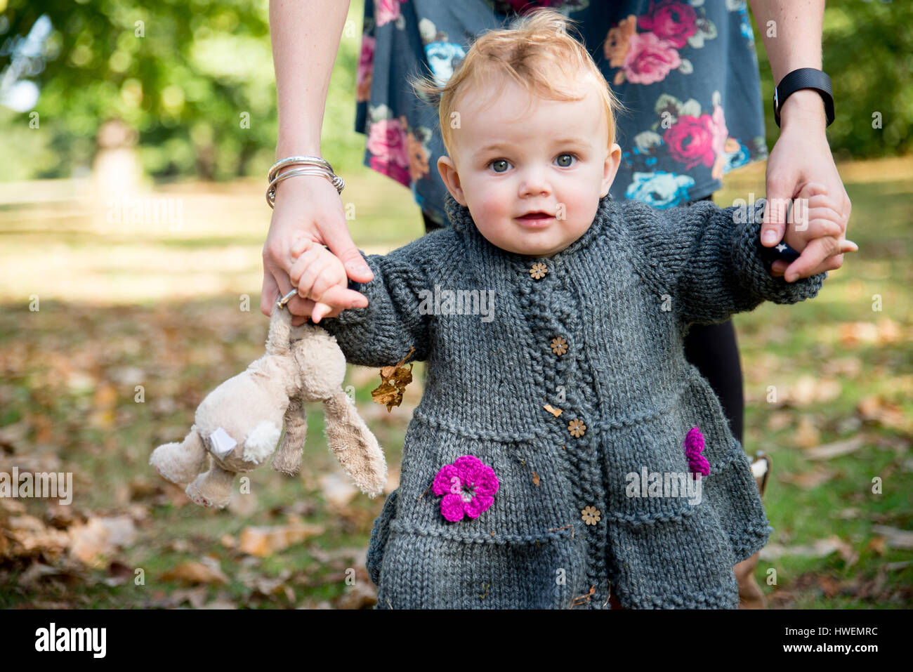 Portrait of baby girl holding mother's hands et d'une façon incertaine dans park Banque D'Images