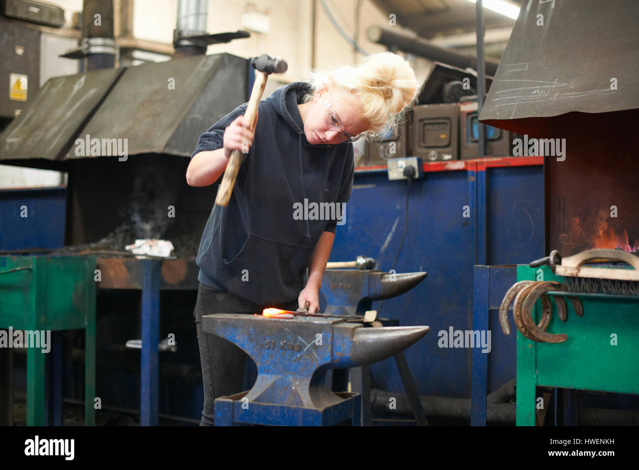 Jeune femme stagiaire blacksmith hammering à cheval sur l'enclume de l'atelier Banque D'Images
