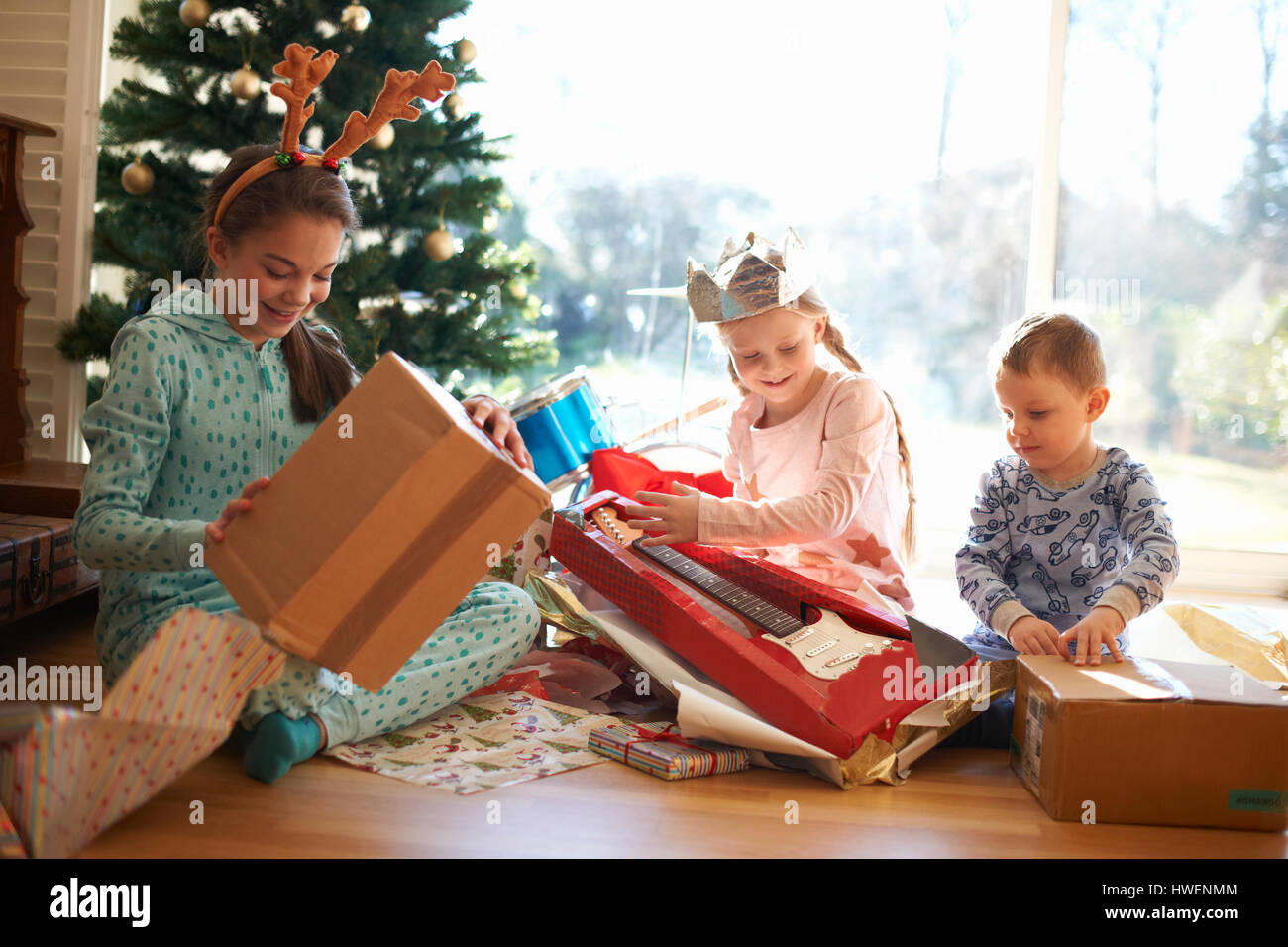 Garçon et soeurs assis sur le plancher du salon de l'ouverture des cadeaux de Noël Banque D'Images