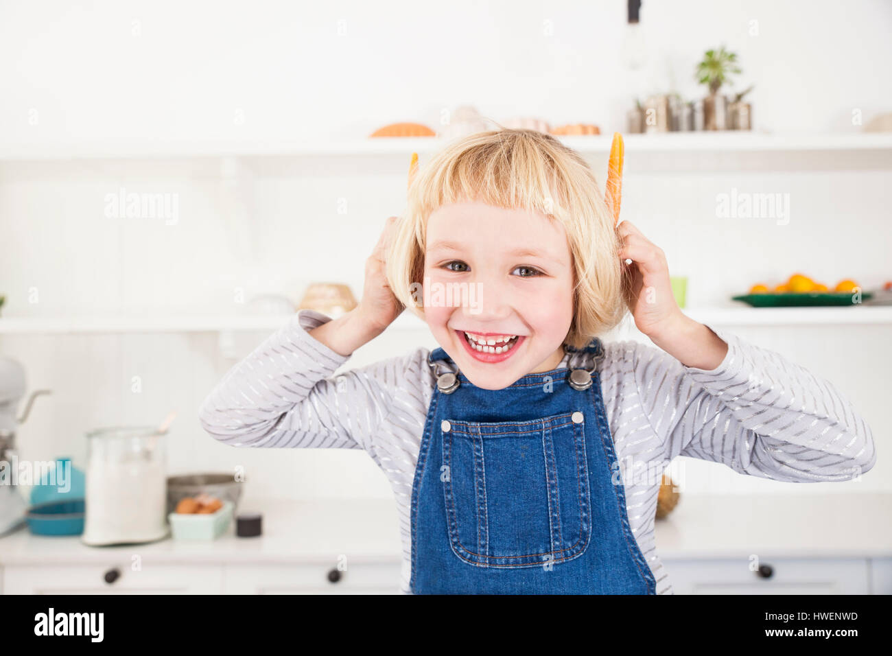 Portrait of cute girl in kitchen holding carrots à ses oreilles Banque D'Images