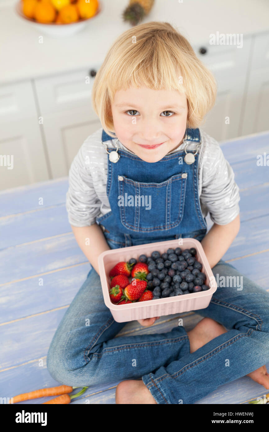 Portrait of cute girl holding punnett de bleuets et fraises à compteur de cuisine Banque D'Images