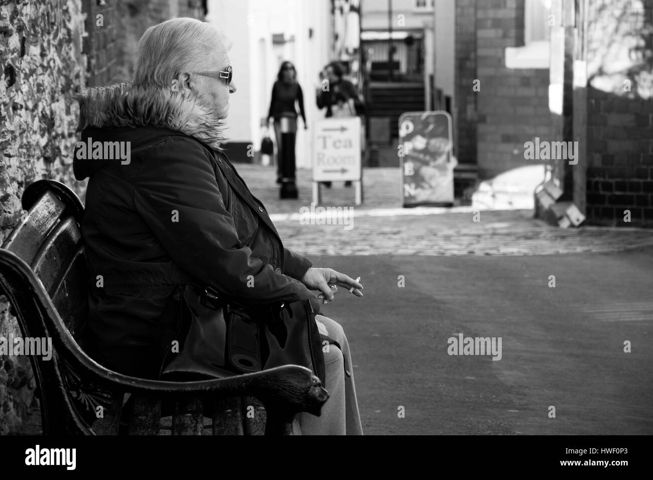 Une vieille femme assis sur un banc, fumant une cigarette. Banque D'Images