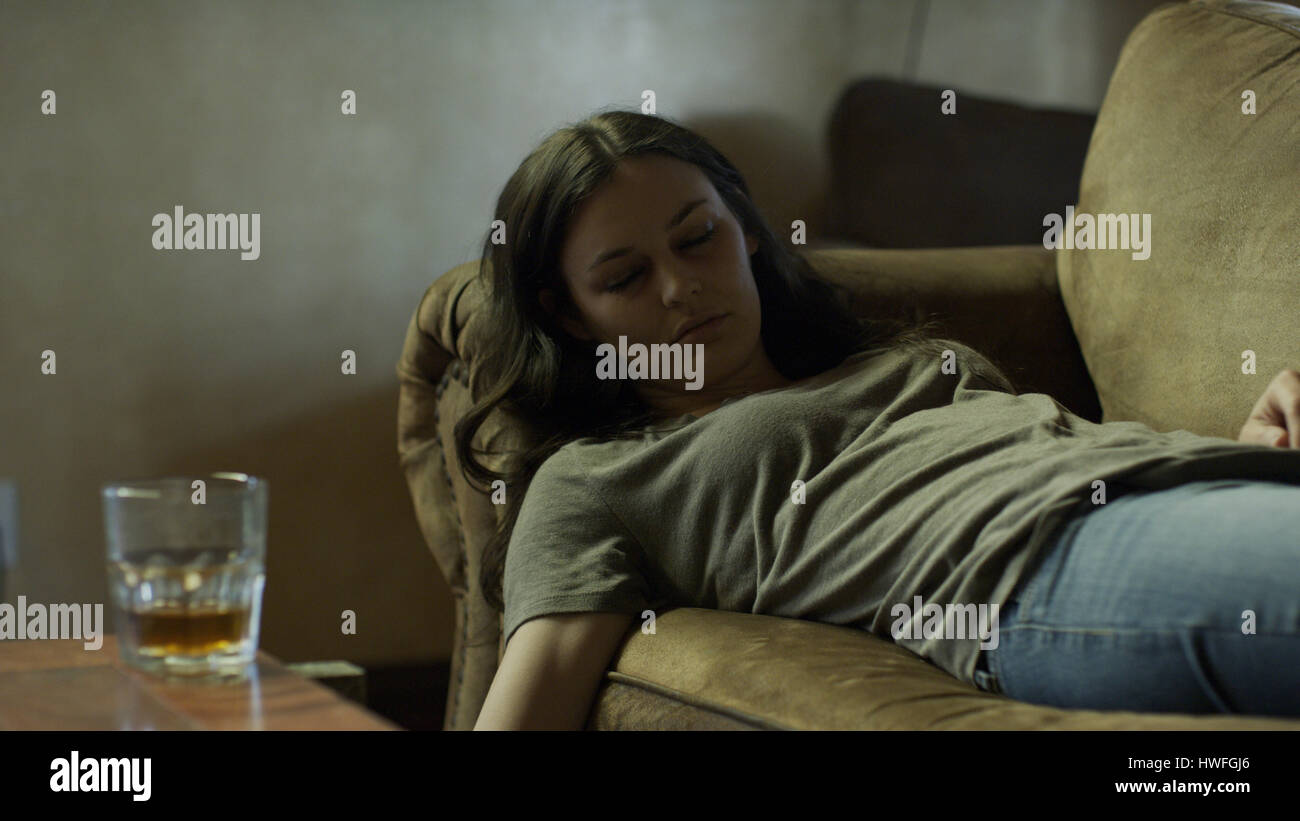 Femme triste dormir près de boisson alcoolisée sur canapé miteux Banque D'Images