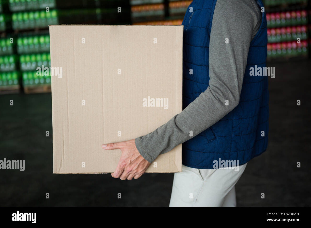 Mid section of worker carrying cardboard box in warehouse Banque D'Images