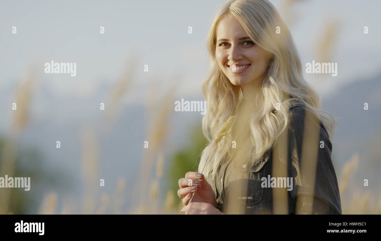 Selective focus view of woman smiling in grass en paysage à distance Banque D'Images