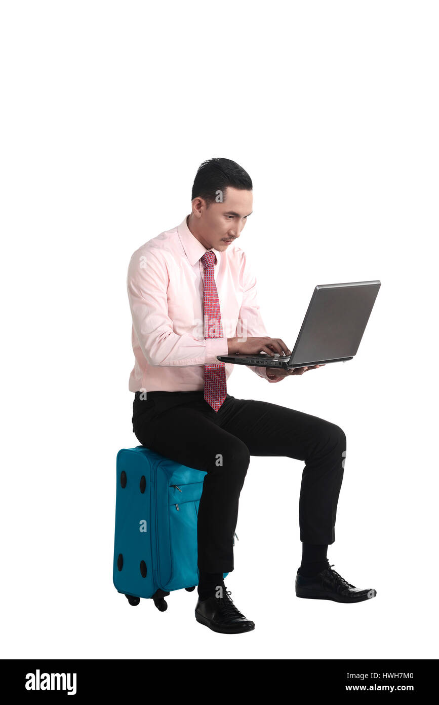 L'homme s'asseoir sur la valise, le travail avec ordinateur portable, isolé sur fond blanc Banque D'Images