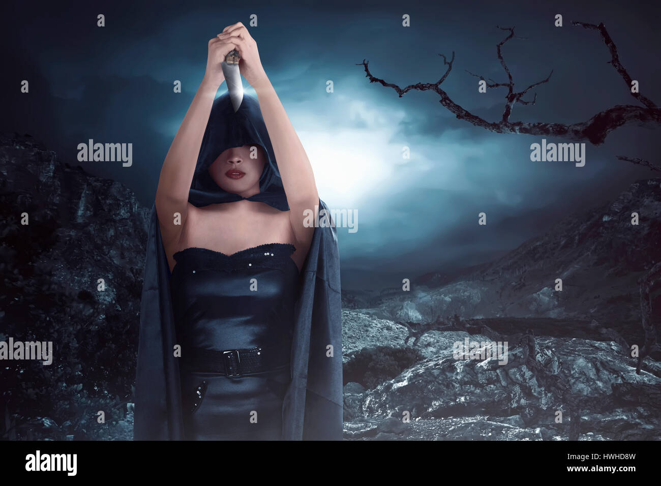 Sorcière femme avec costume noir portant cape et la holding couteau sur la rock hills au minuit Banque D'Images