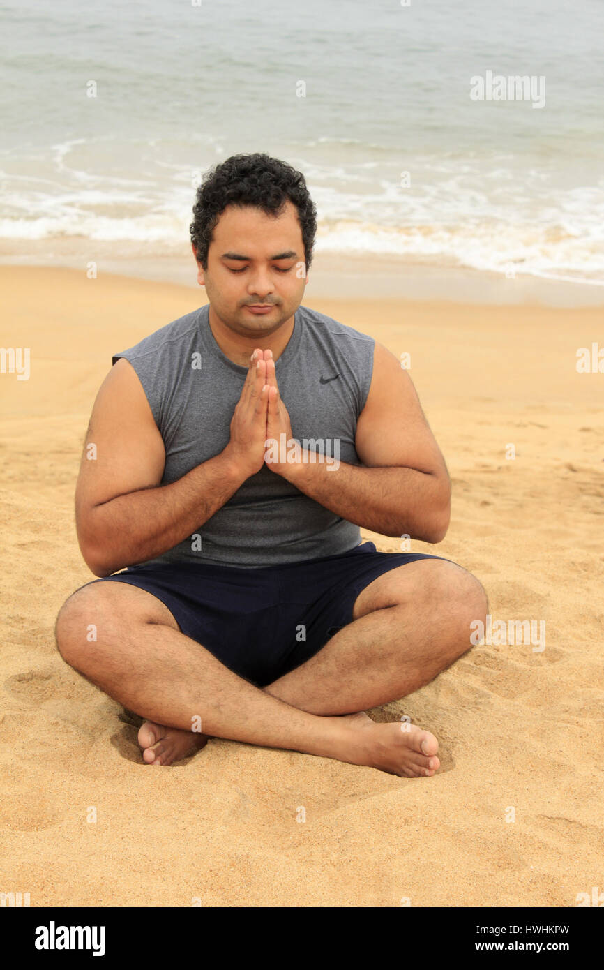 Homme assis sur la plage avec des jambes croisées , priant position, mains jointes et les yeux
