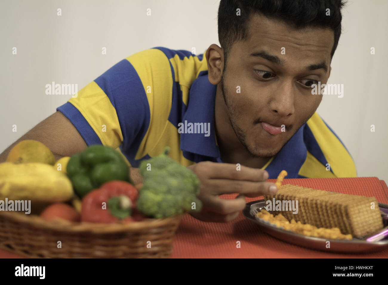 L'envie l'homme sucré salé des aliments malsains sur le panier de légumes et fruits sains Banque D'Images