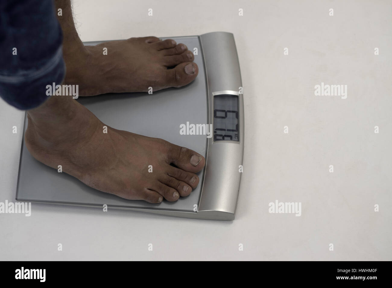 Homme debout sur l'échelle de pesage numérique montrant 67,8 kg Banque D'Images