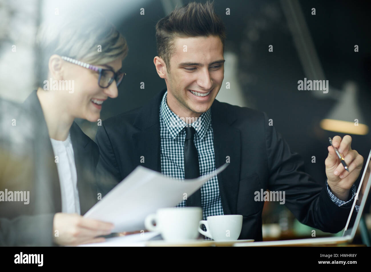 De jeunes collègues joyeuse à la recherche à l'écran de l'ordinateur pendant l'analyse de résultats de projet accompli, vue à travers la fenêtre cafe Banque D'Images