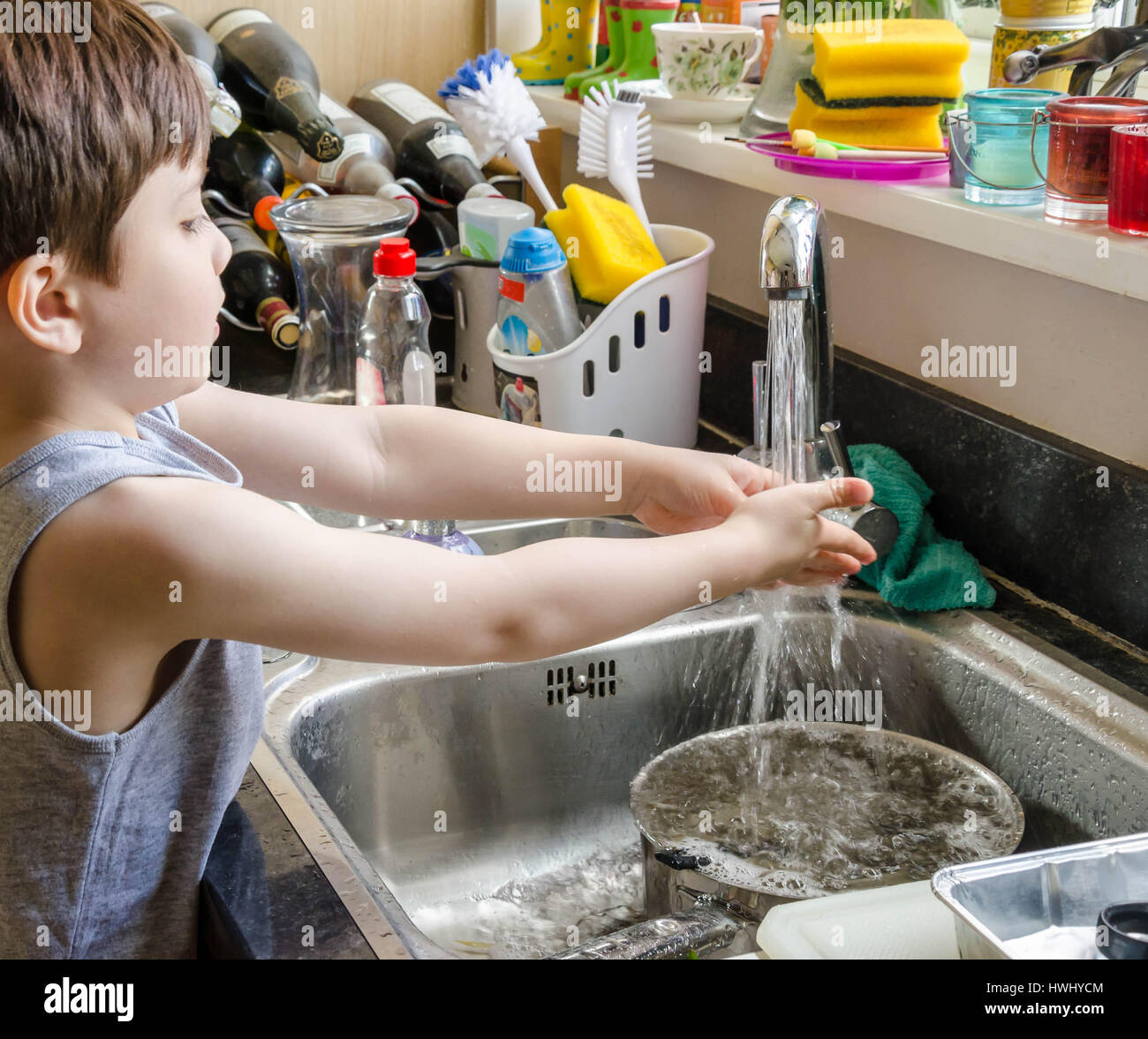 Un jeune garçon se lave les mains sous le robinet d'évier de cuisine. Banque D'Images