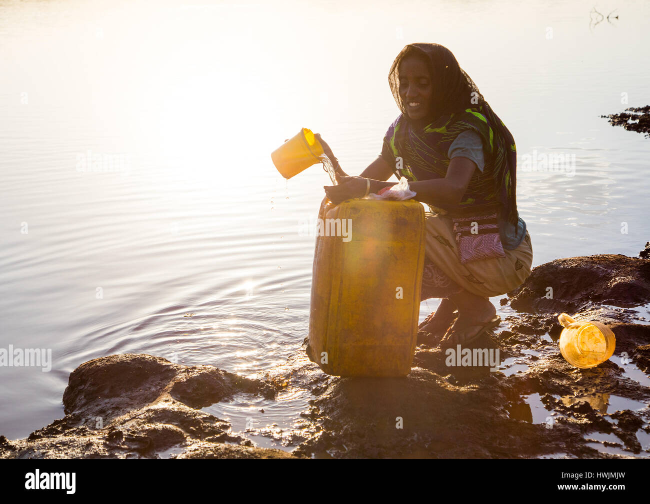 Femme de la tribu Borana jerricanes de remplissage dans un réservoir d'eau utilisé pour les animaux, Oromia, Yabelo,, Ethiopie Banque D'Images