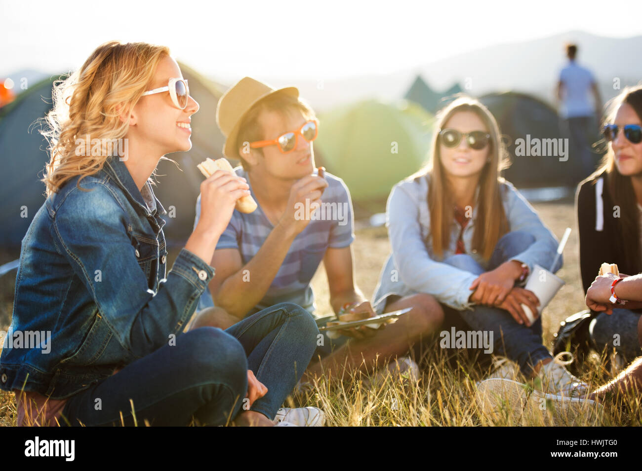 Groupe de jeunes garçons et filles à summer music festival, assis sur le sol en face de tentes de manger Banque D'Images