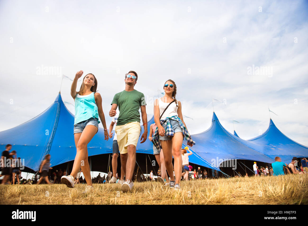Groupe de jeunes garçons et filles à summer music festival balade en face de big blue tente, journée ensoleillée Banque D'Images