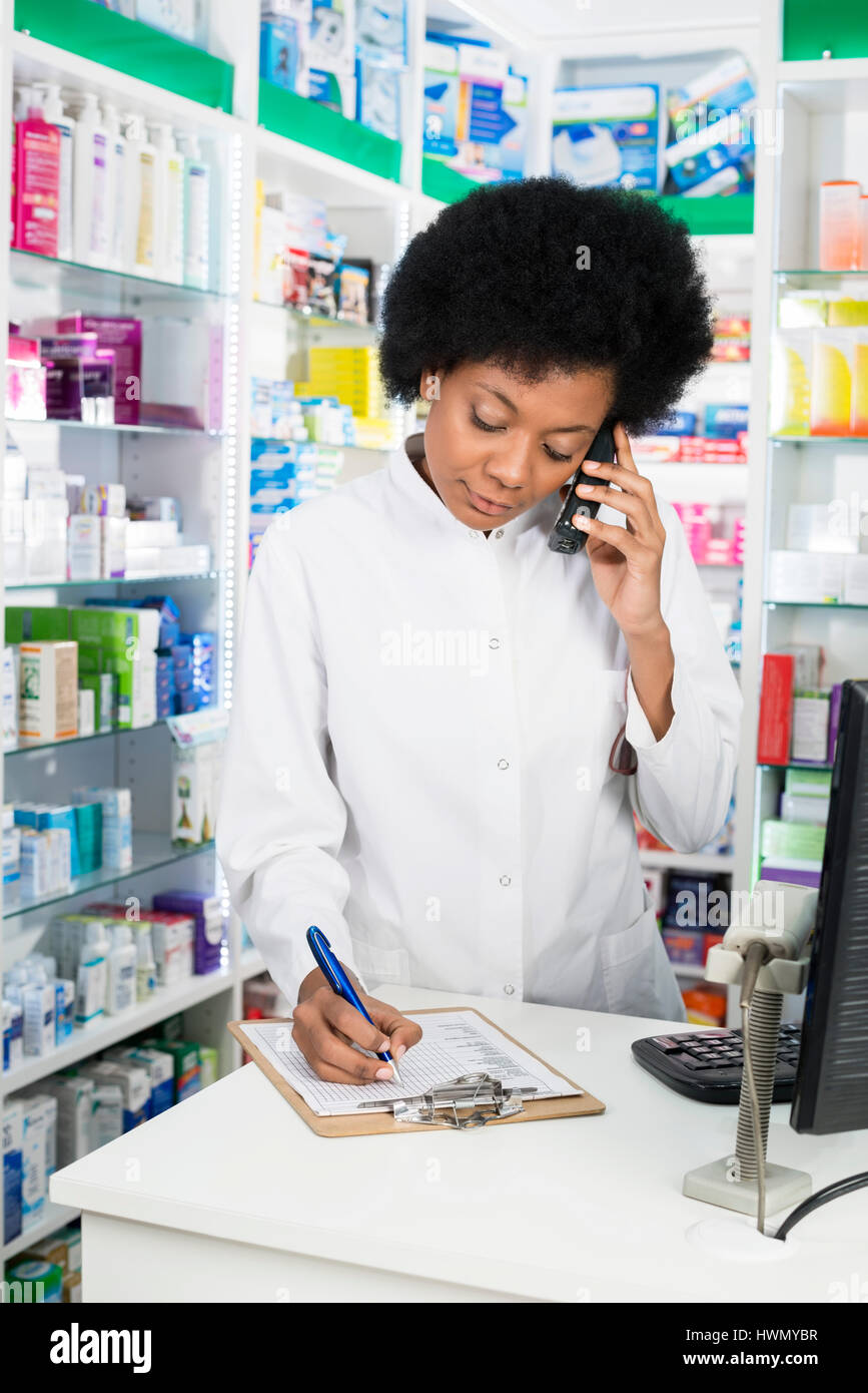 Pharmacien Writing On Clipboard lors de l'utilisation de téléphone sans fil Banque D'Images