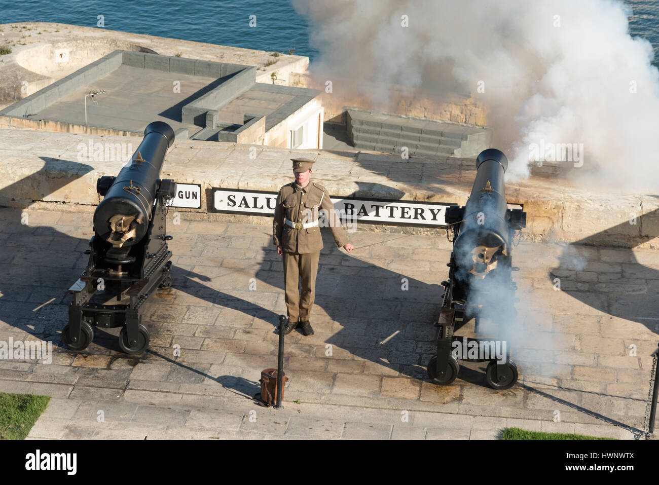 Un soldat en uniforme le tir d'un canon à la batterie de salut à La Valette Malte overlookingthe Grand Port pour le quotidien salue Banque D'Images