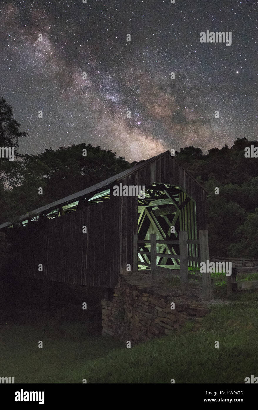 Le vieux pont couvert en bois à Locust Creek près de Hillsboro, West Virginia est en dessous de la voie lactée sur une sombre nuit claire, la lueur d'une lumière à l'intérieur. Banque D'Images