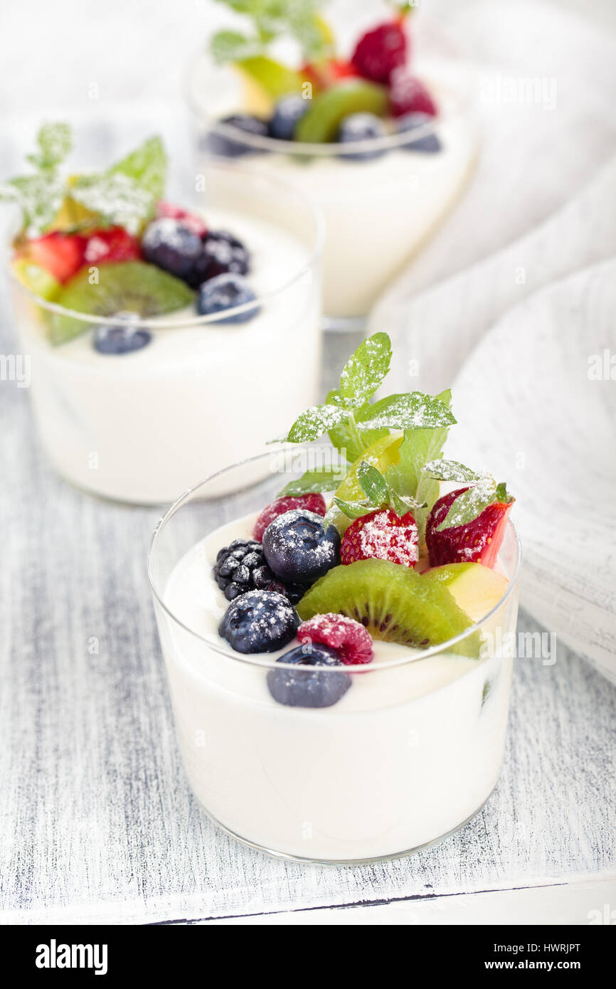 Yaourt frais aux fruits rouges. On white table rustique. Se concentrer sur les feuilles de menthe et de bleuet et de kiwis dans le centre du premier verre. Banque D'Images