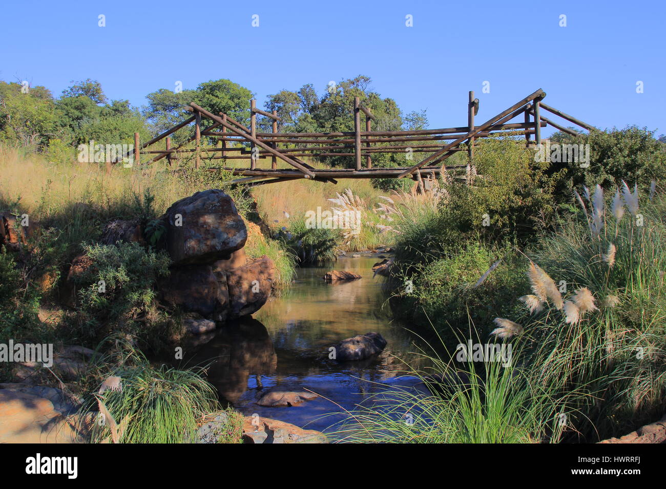 Un paisible ruisseau serpente à travers la campagne tranquille avec un pont à pied en bois et d'un ciel bleu clair Banque D'Images