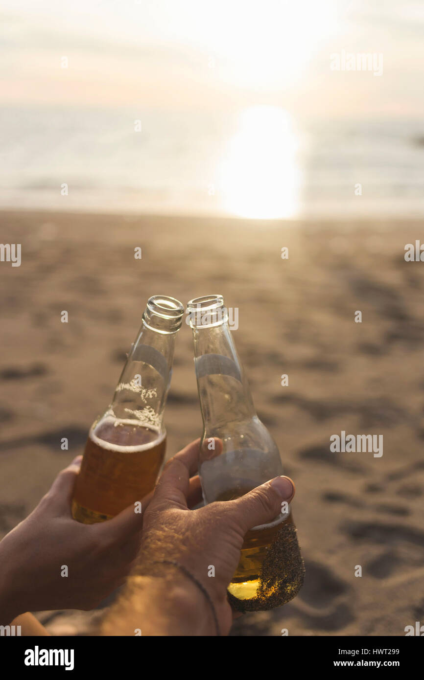 Les mains coupées de friends toasting beer à la plage pendant le coucher du soleil Banque D'Images