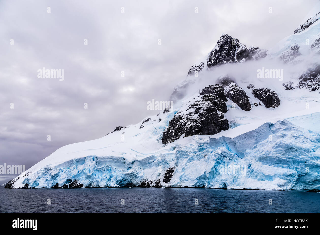 Raide énorme rocher de pierre recouverte de glaciers bleu et de nuages avec de l'eau en premier plan, près d'îles Argentines, croisière de l'Antarctique Banque D'Images