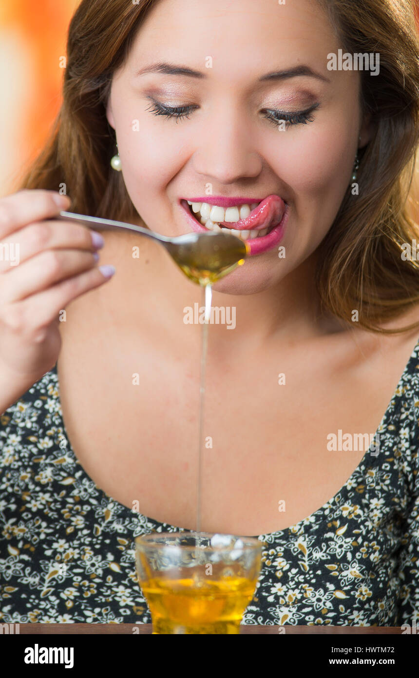 Young woman holding spoon caméra avec du miel en petites gouttes sur la table en verre Banque D'Images