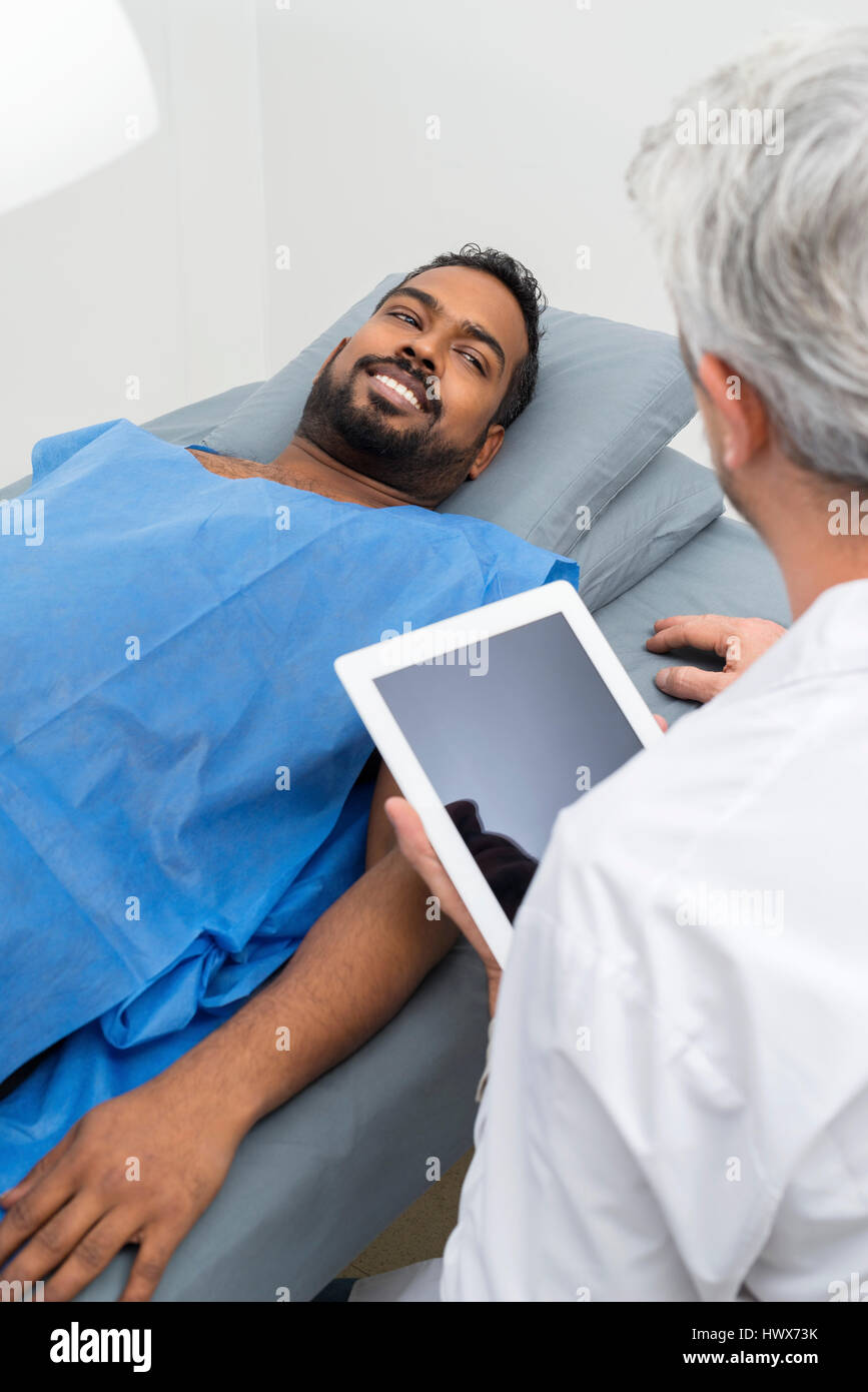Mâle mature radiologue using digital tablet par patient lying on hospital bed Banque D'Images