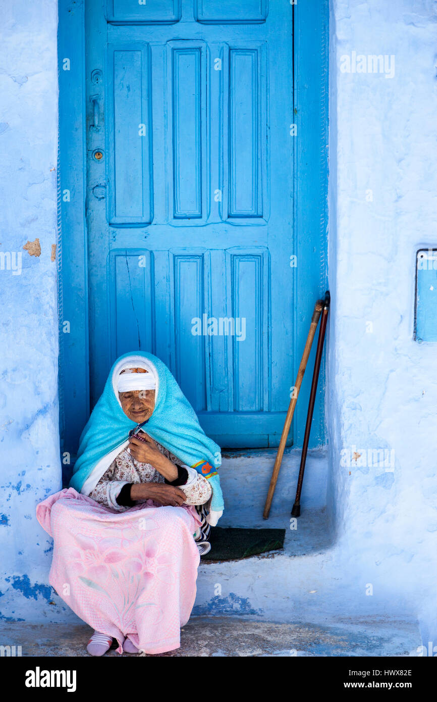 Chefchaouen, Maroc. Vieille Femme en costume traditionnel berbère assis sur sa porte. Banque D'Images