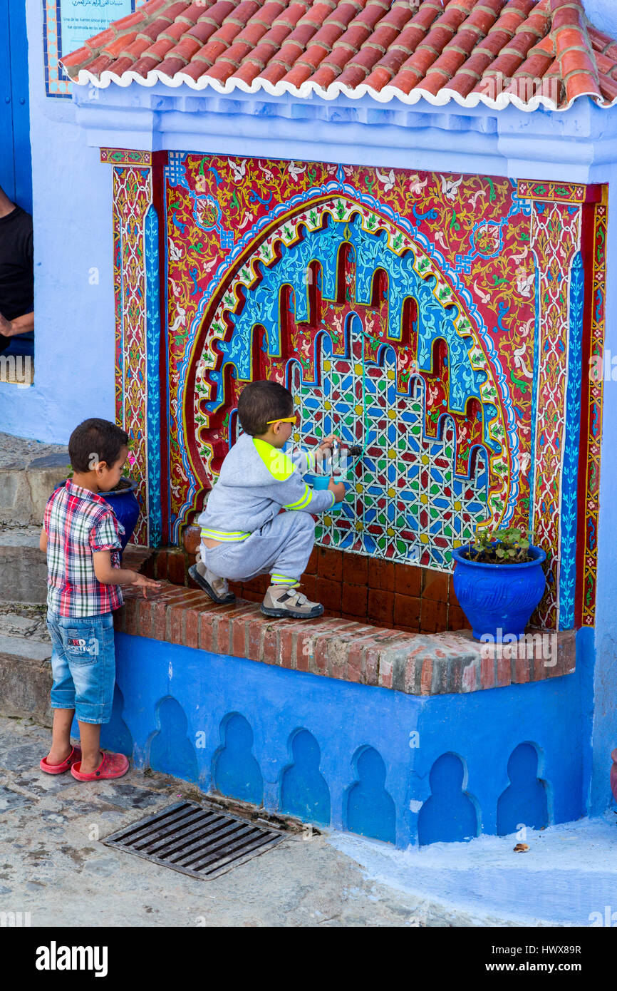 Chefchaouen, Maroc. Deux jeunes garçons obtenir de l'eau à un robinet d'eau public. Banque D'Images