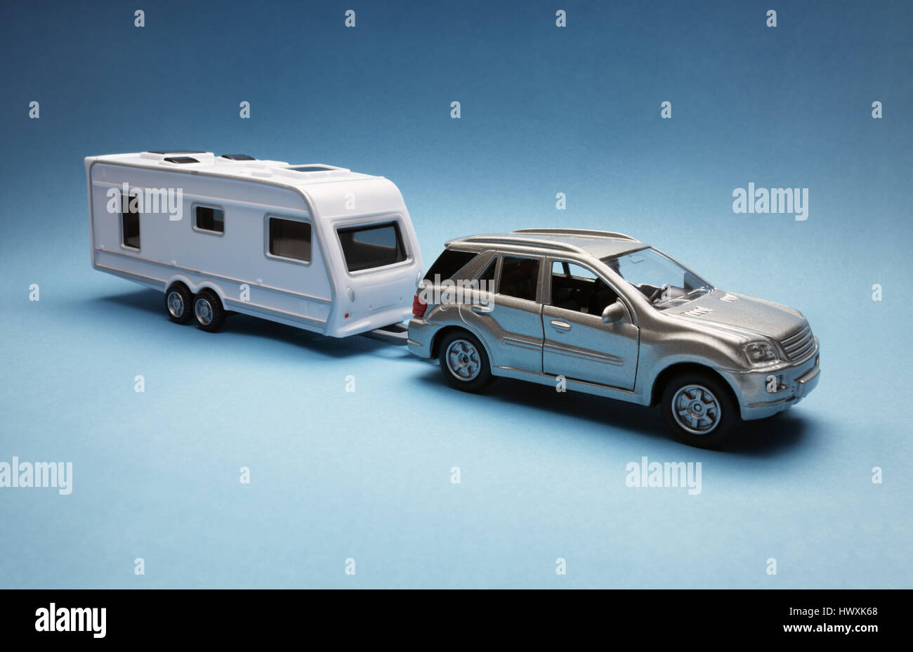 Petite voiture tractant une caravane de conception générique sur fond bleu Banque D'Images