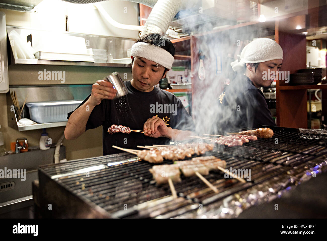 Vendeur d'aliments de rue l'assaisonnement des bâtons de viande dans une rue au Japon. Banque D'Images