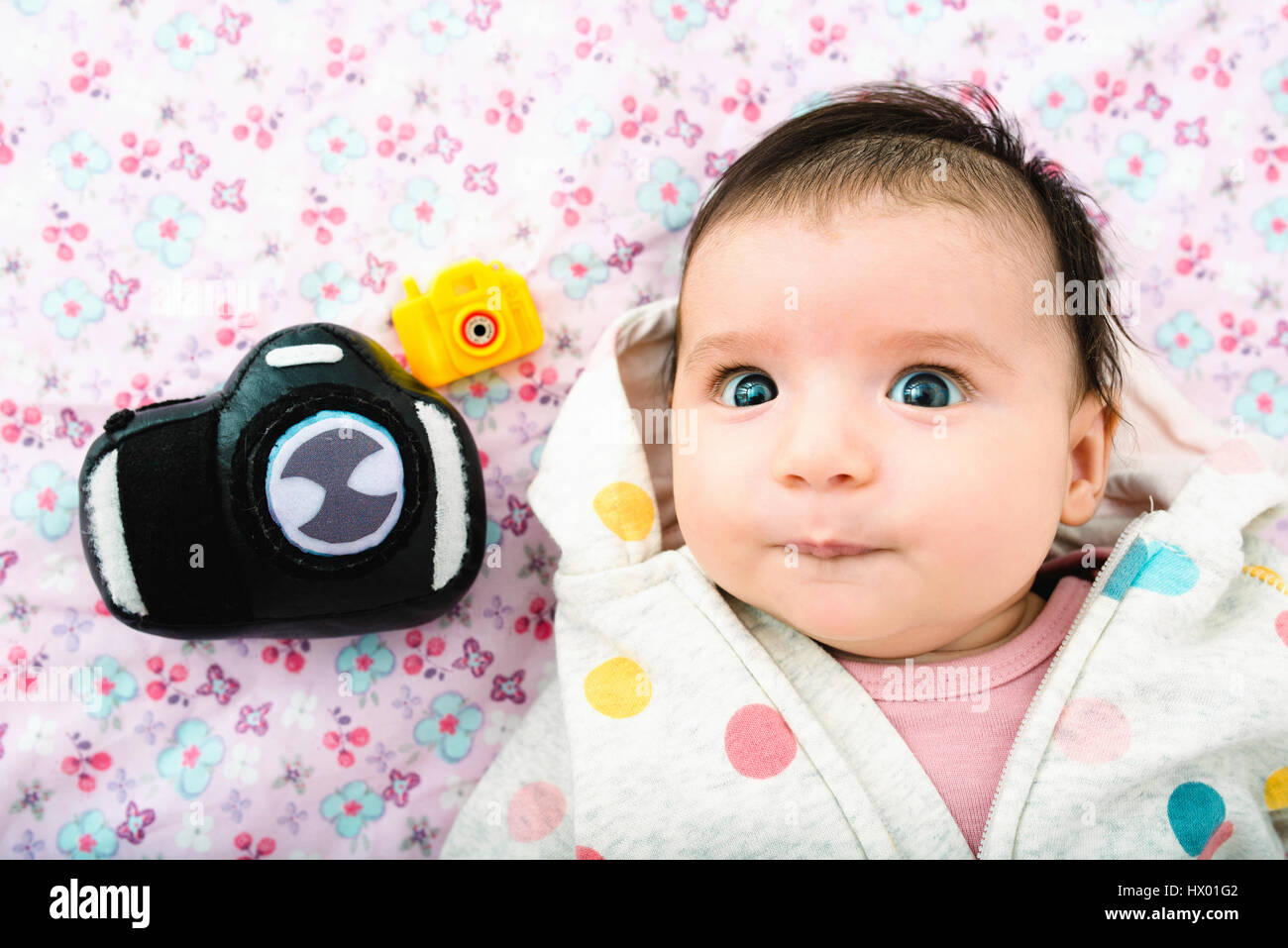 Portrait of baby girl lying on bed avec deux caméras jouets Banque D'Images