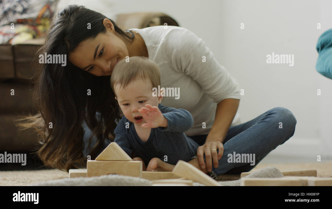 Mère et bébé curieux fils assis sur le plancher et en jouant avec les blocs de construction Banque D'Images