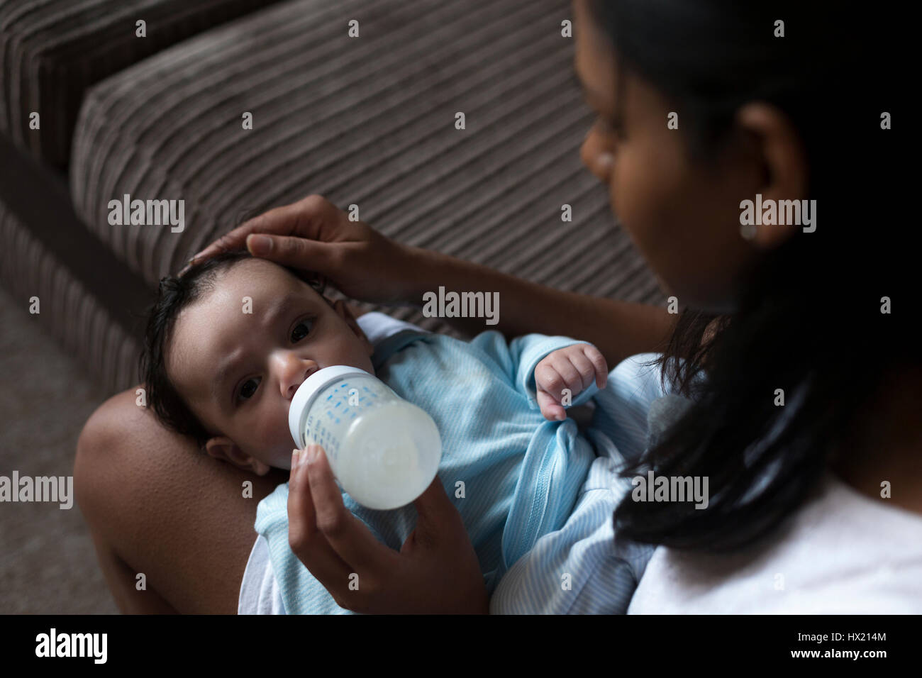 Jeune mère est assise avec son bébé sur ses genoux. Elle est l'alimentation de lui une bouteille de lait. Banque D'Images