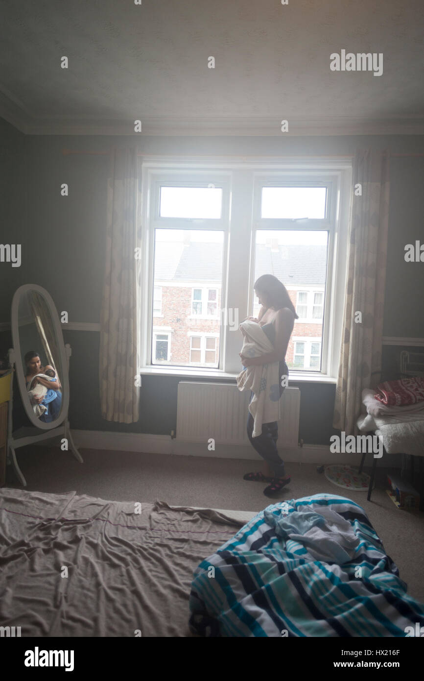 Jeune mère debout dans sa chambre près de la fenêtre avec son fils bébé endormi dans ses bras. Banque D'Images