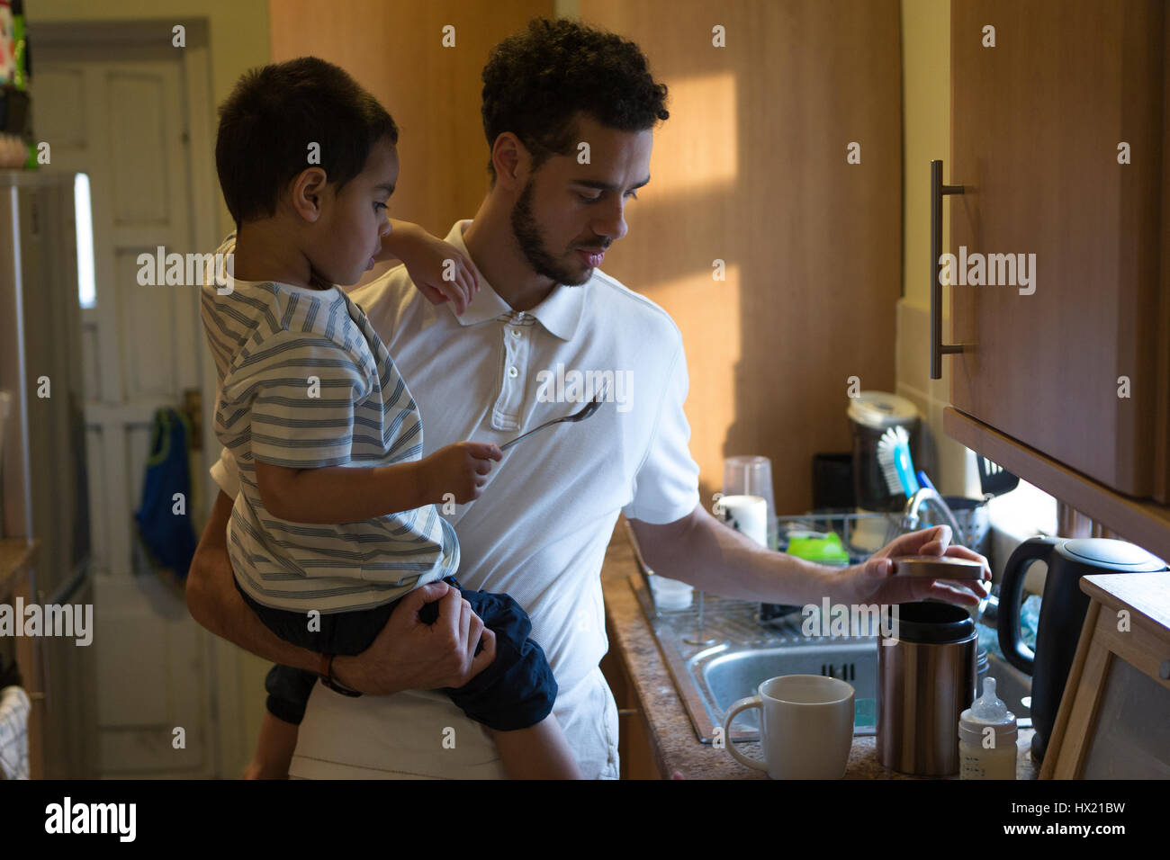 Jeune père de prendre une tasse de thé avec l'aide de son fils. Il est l'ouverture d'un pot de sucre et le petit garçon est maintenant la cuillère. Banque D'Images