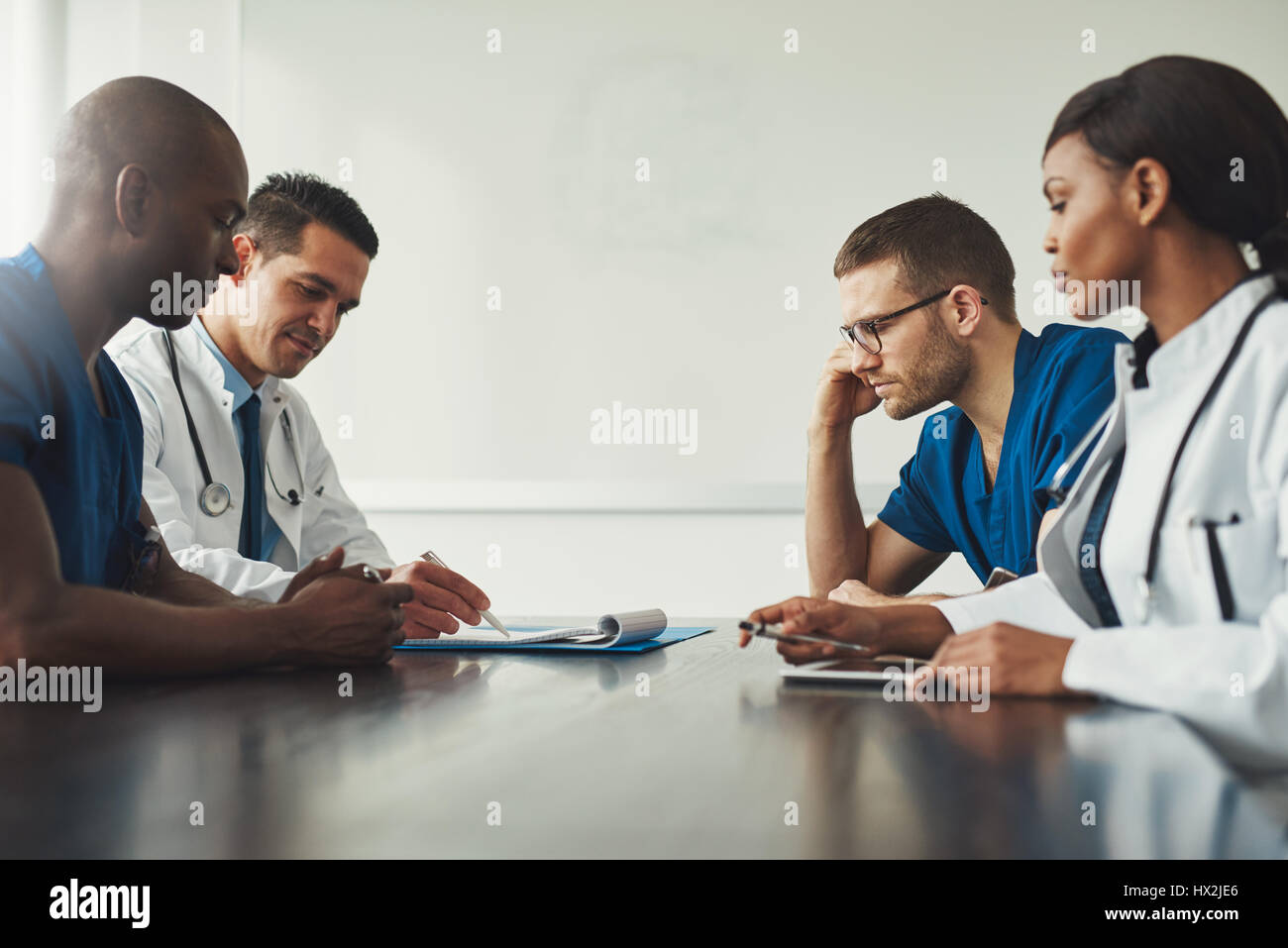 Réunion du personnel médical. Groupe de jeunes gens en blouse blanche et uniforme bleu assis à table en face de l'autre. Vue latérale avec un angle faible copie sp Banque D'Images
