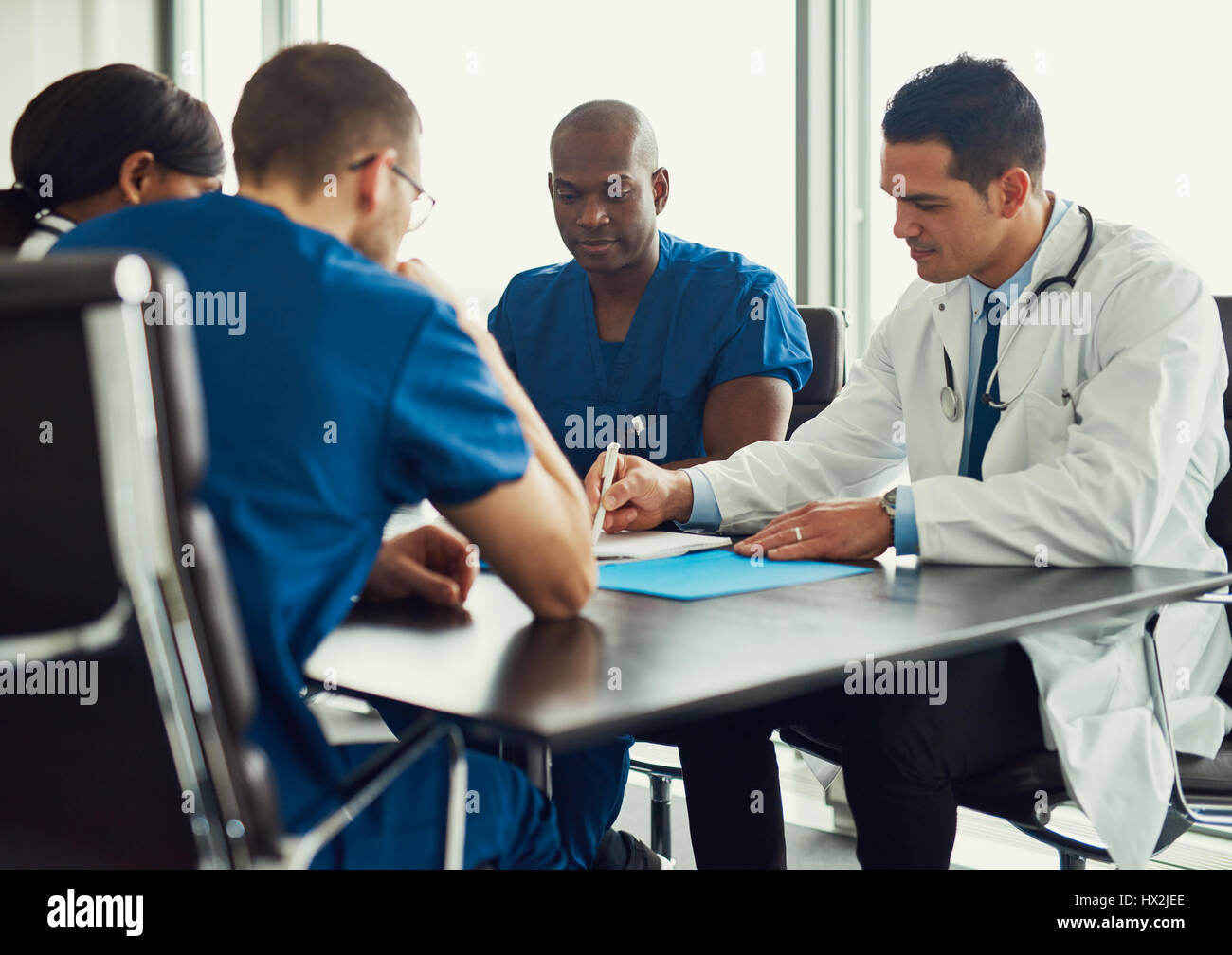 Les jeunes sur le personnel médical, rencontre avec l'homme en blouse blanche montrant quelque chose dans le journal, assis à table dans cette chambre lumineuse Banque D'Images