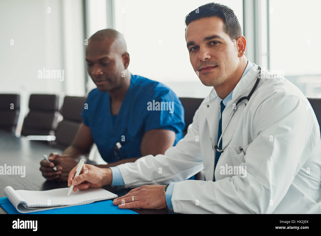 Jeune homme médecin en blouse blanche avec stéthoscope sur son cou, assis à table de salle de conférence. Médecin homme afro-américains en bleu Banque D'Images